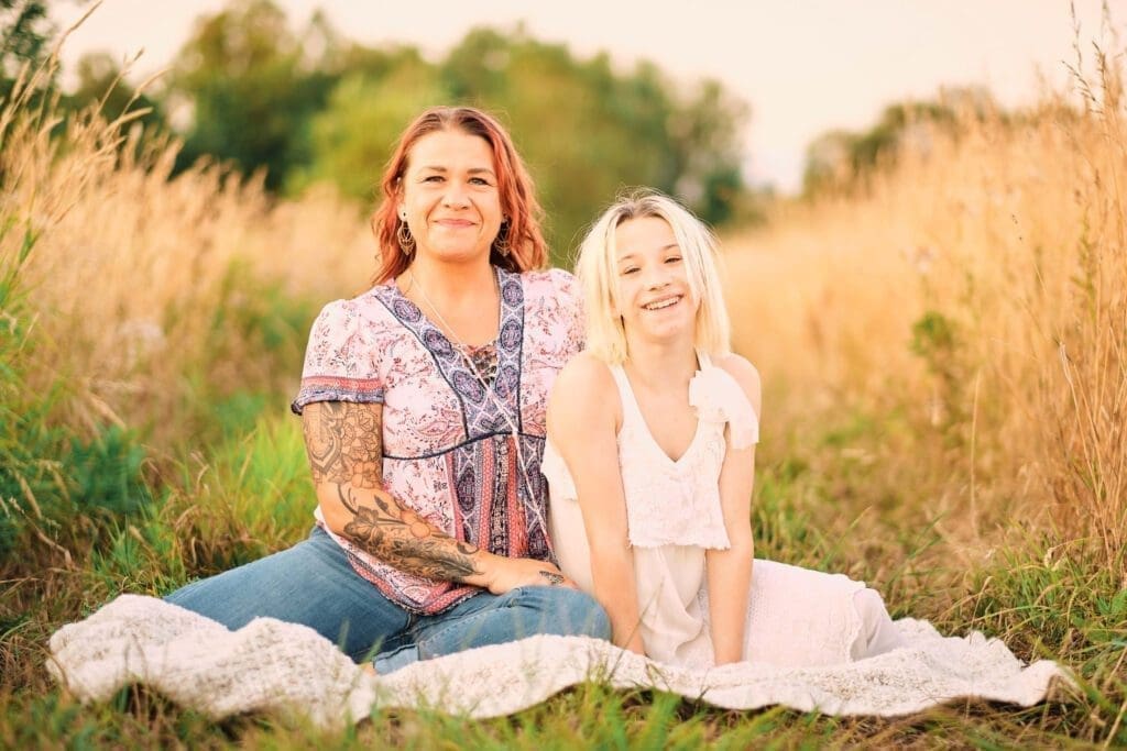 Mother and daughter sitting on a blanket amongst tall grasses at sunset.