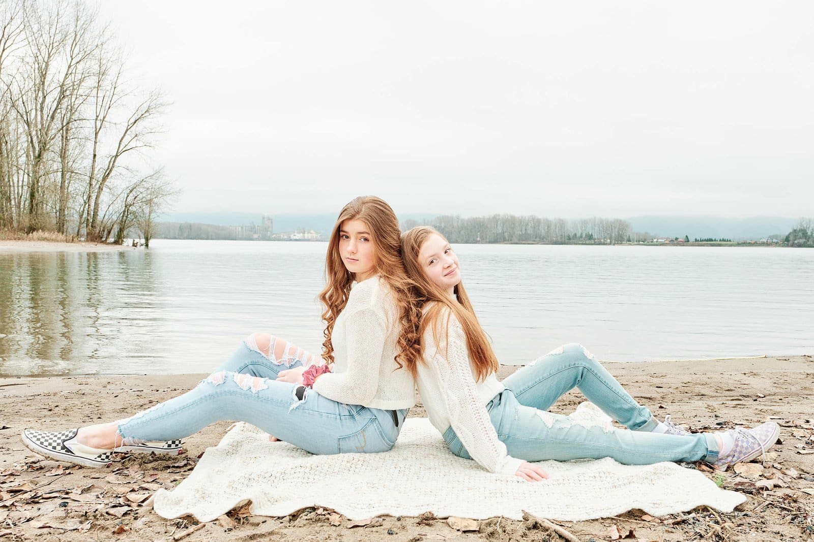 Two sisters sitting on a blanket on a beach near the Columbia River in Vancouver, Washington.